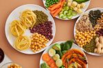 A vibrant mix of legumes, vegetables, nuts, and pasta arranged on white plates showcasing a balanced, healthy diet.